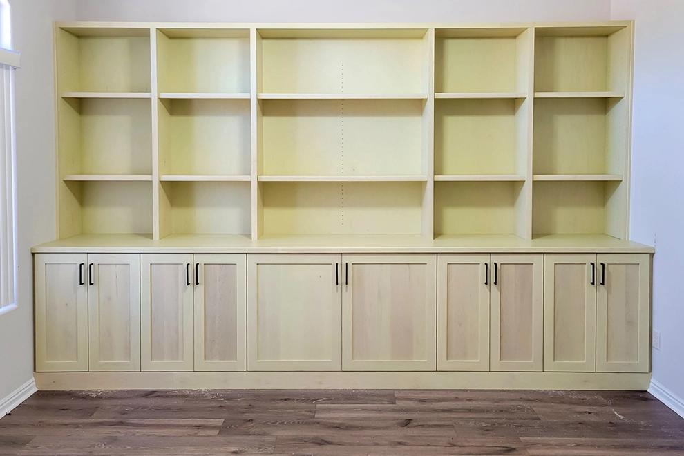 Custom-designed wall-to-wall bookcase, stretching over 13 feet with five individual sections featuring cabinets at the bottom and adjustable shelves above. Central section is notably wider than others.